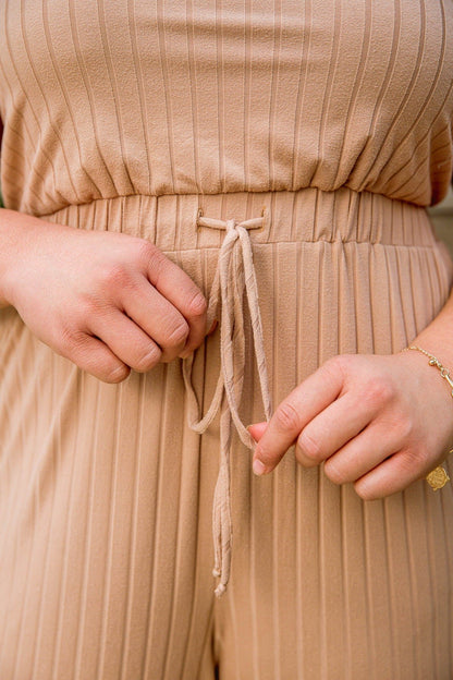 Model wearing Cruiser Jumpsuit in Tan, close-up view, available at J&J Shop Online.