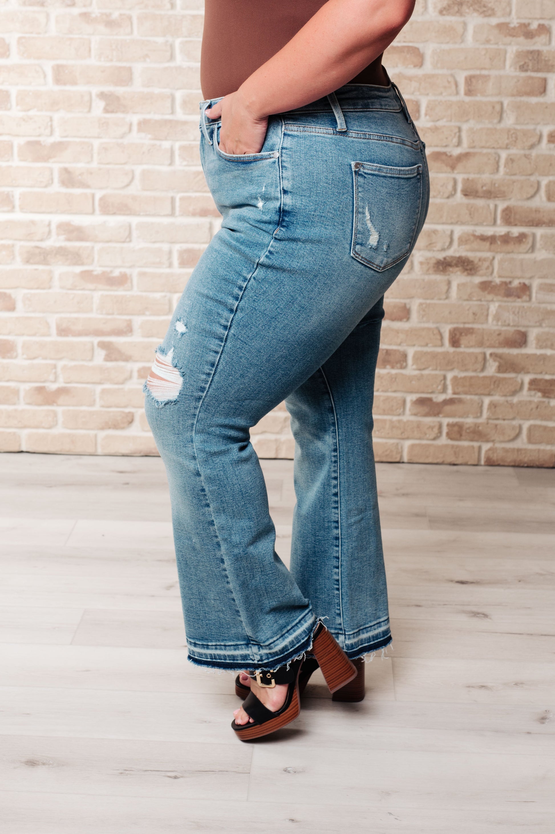 Close-up of model wearing Isla Mid Rise Distressed Released Hem Bootcut Jeans from J&J Shop Online.