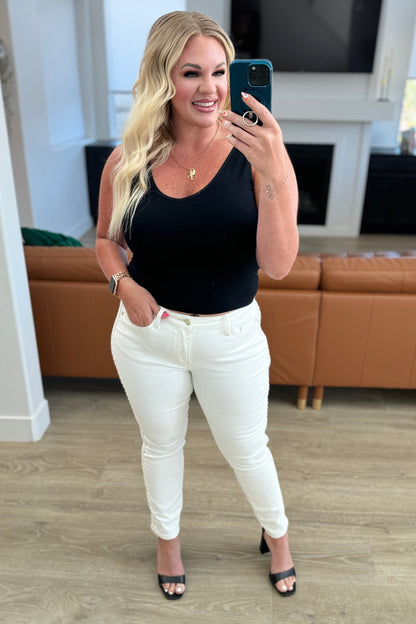 Model Jessica from 90 Day Fiancé wearing Maddie Mid Rise Jeans by Judy Blue, showcasing the front view with braided side seam detail, available at J&J Shop Online.